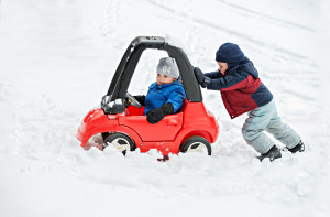 Boy pushing brother's toy car in the snow